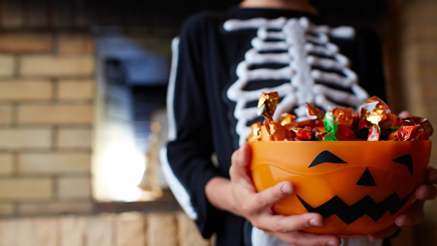 kid in skeleton costume holding jack-o-lantern bowl of candy