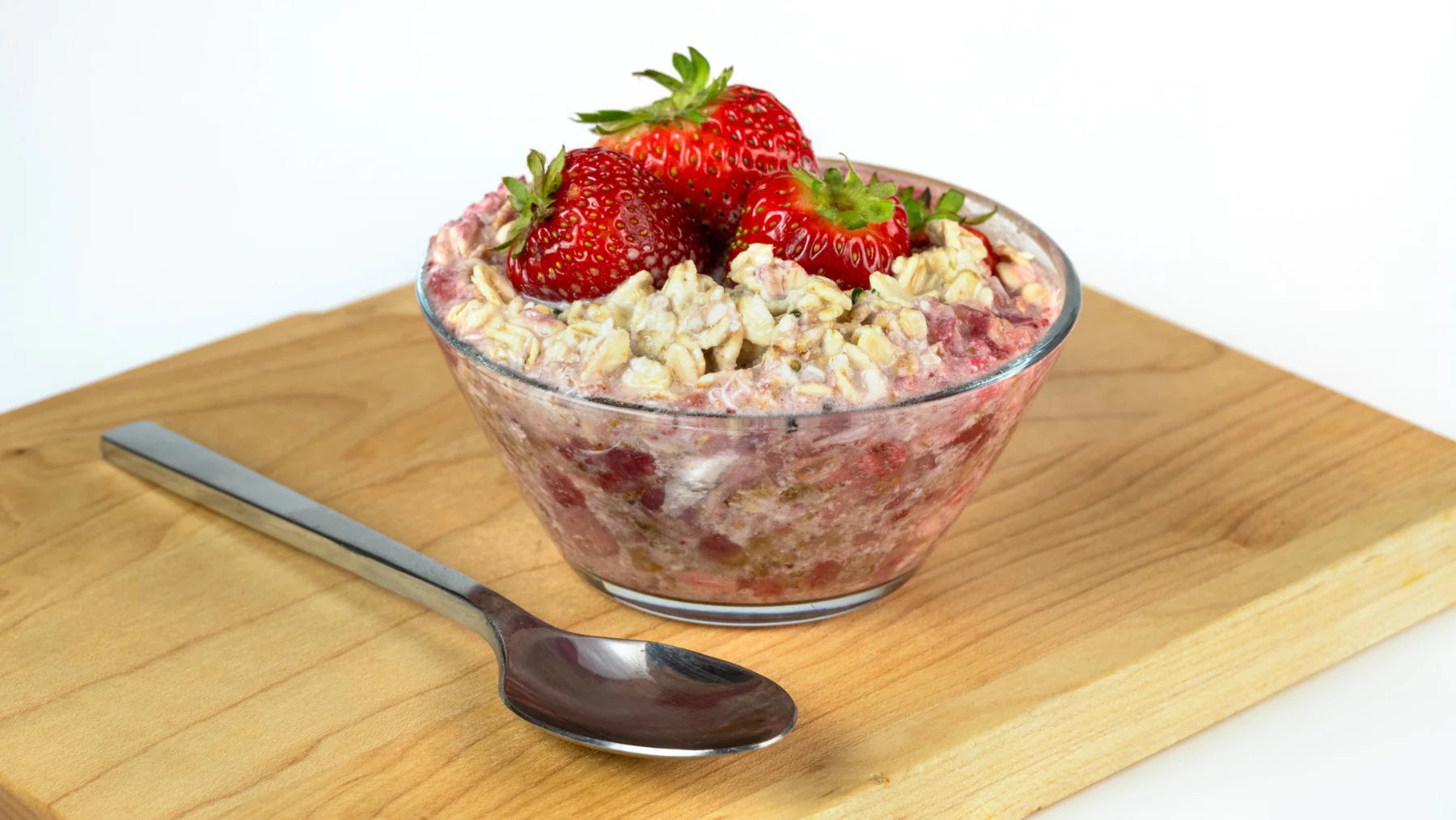 strawberry overnight oats in a glass bowl on a wood cutting board with a spoon laying next to the bowl