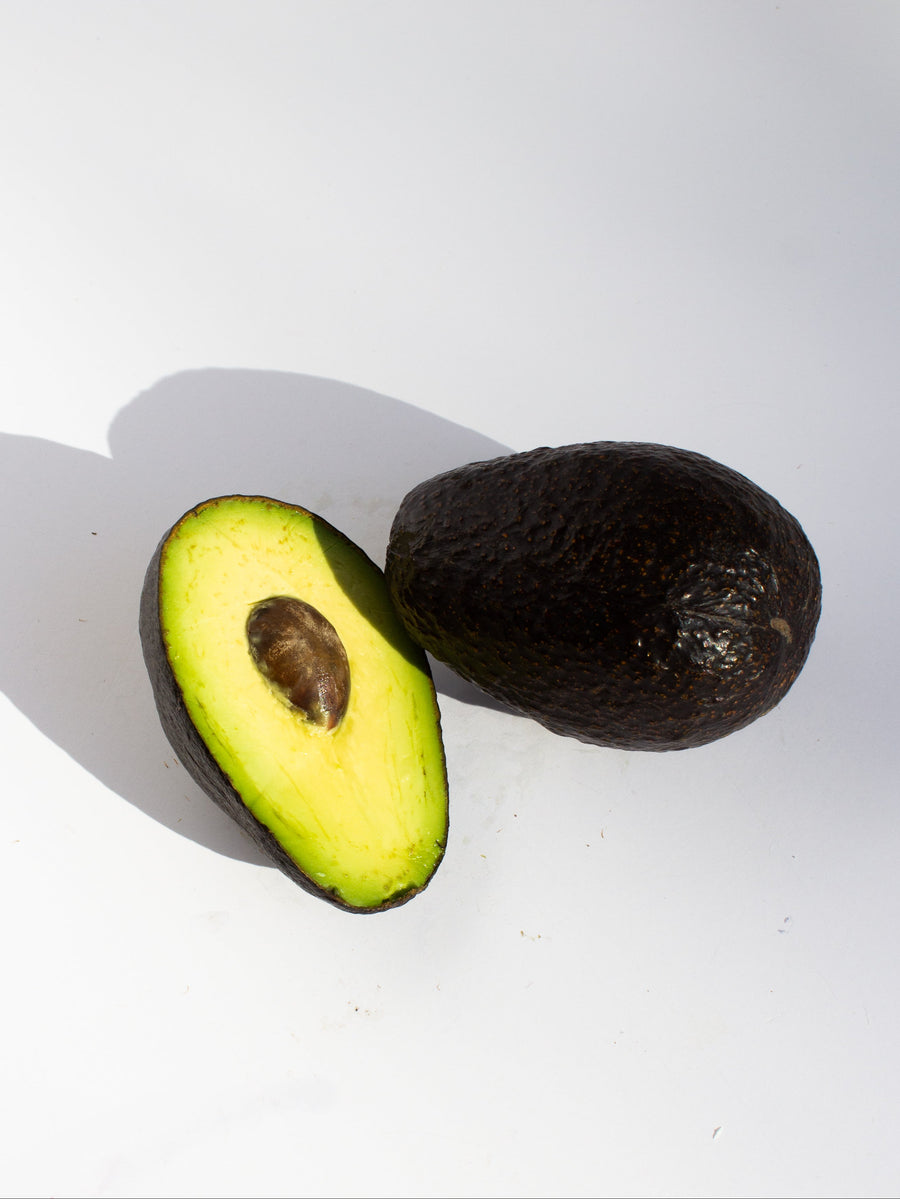Whole avocado next to a sliced half showing the pit and bright green flesh