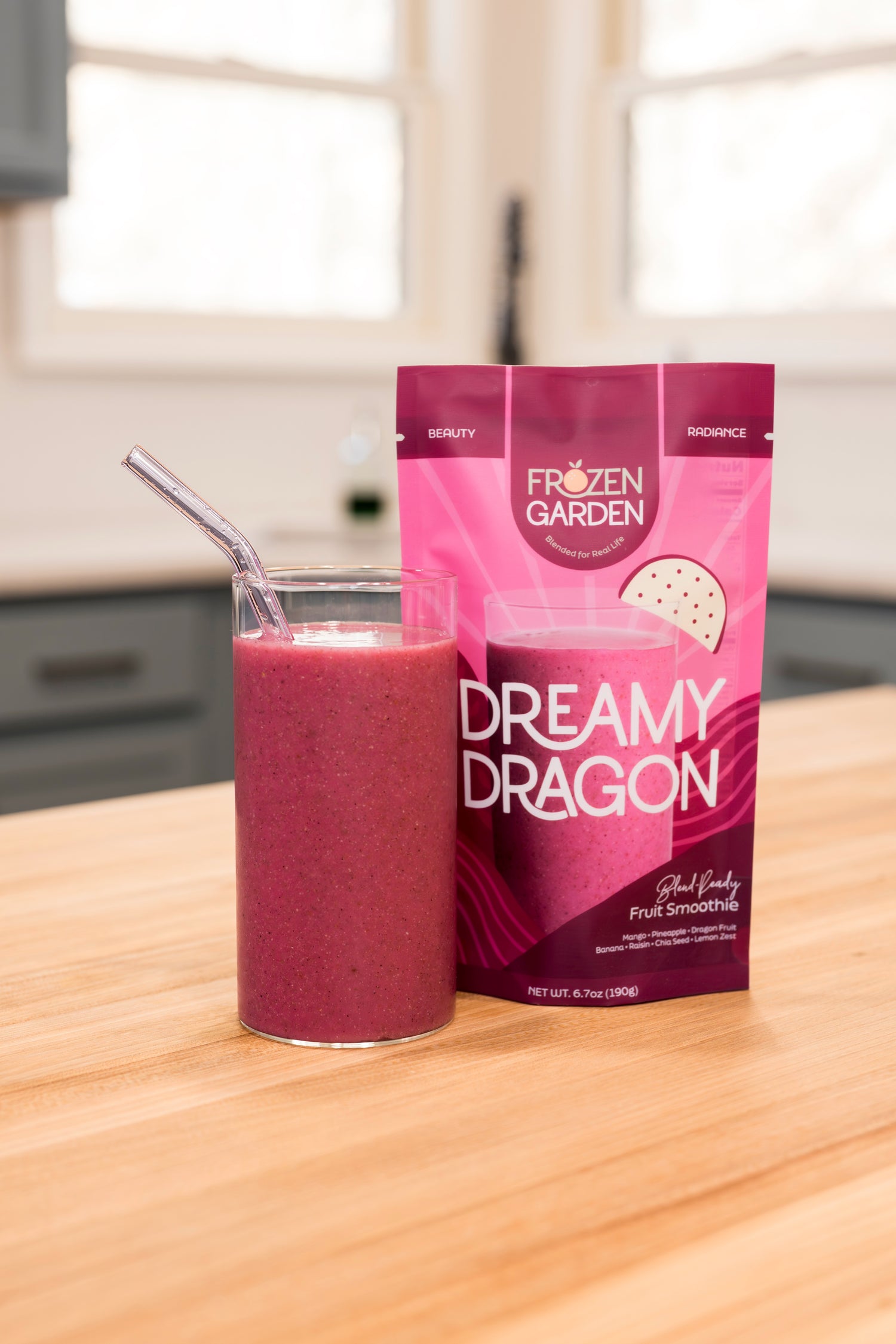Frozen Garden Dreamy Dragon smoothie package with a glass of pink smoothie on a wooden surface.