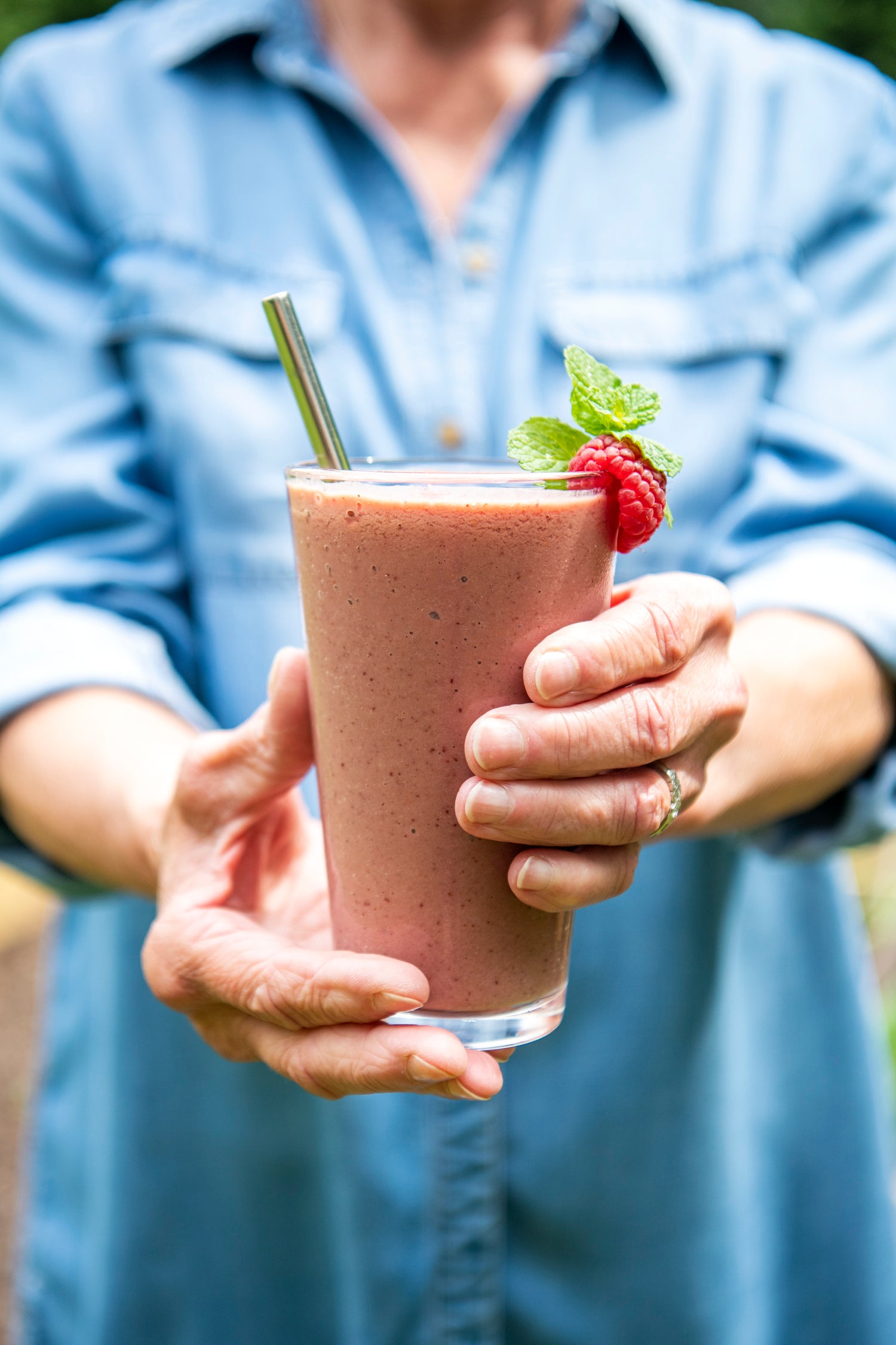 Person holding a pink smoothie with a raspberry and mint leaf garnish.