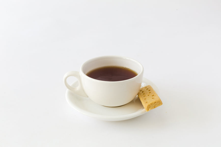 A white cup of black tea and a shortbread cookie on a white saucer.