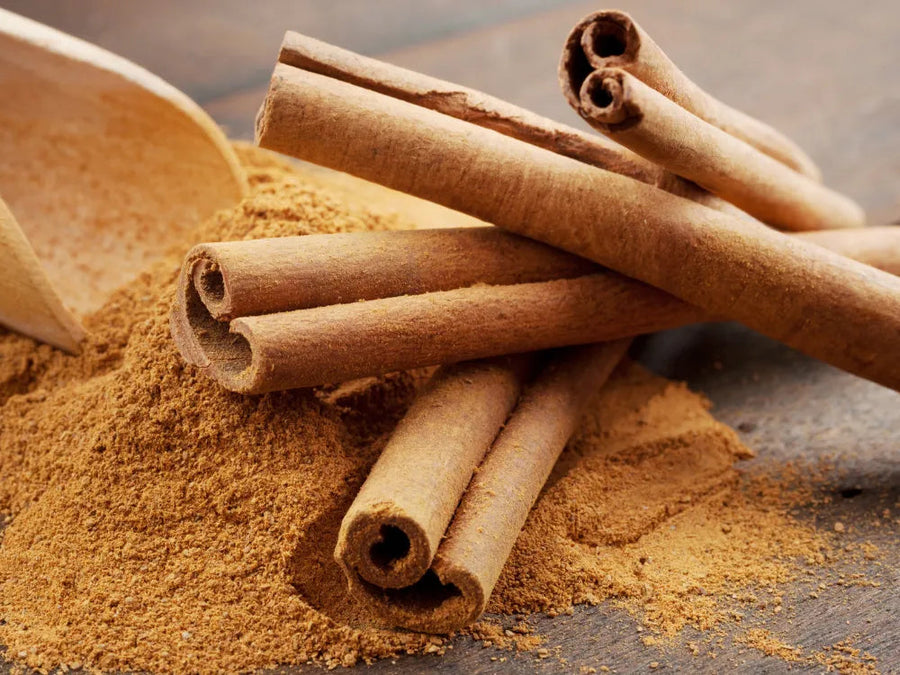 A close-up of whole cinnamon sticks stacked on top of a mound of ground cinnamon powder.