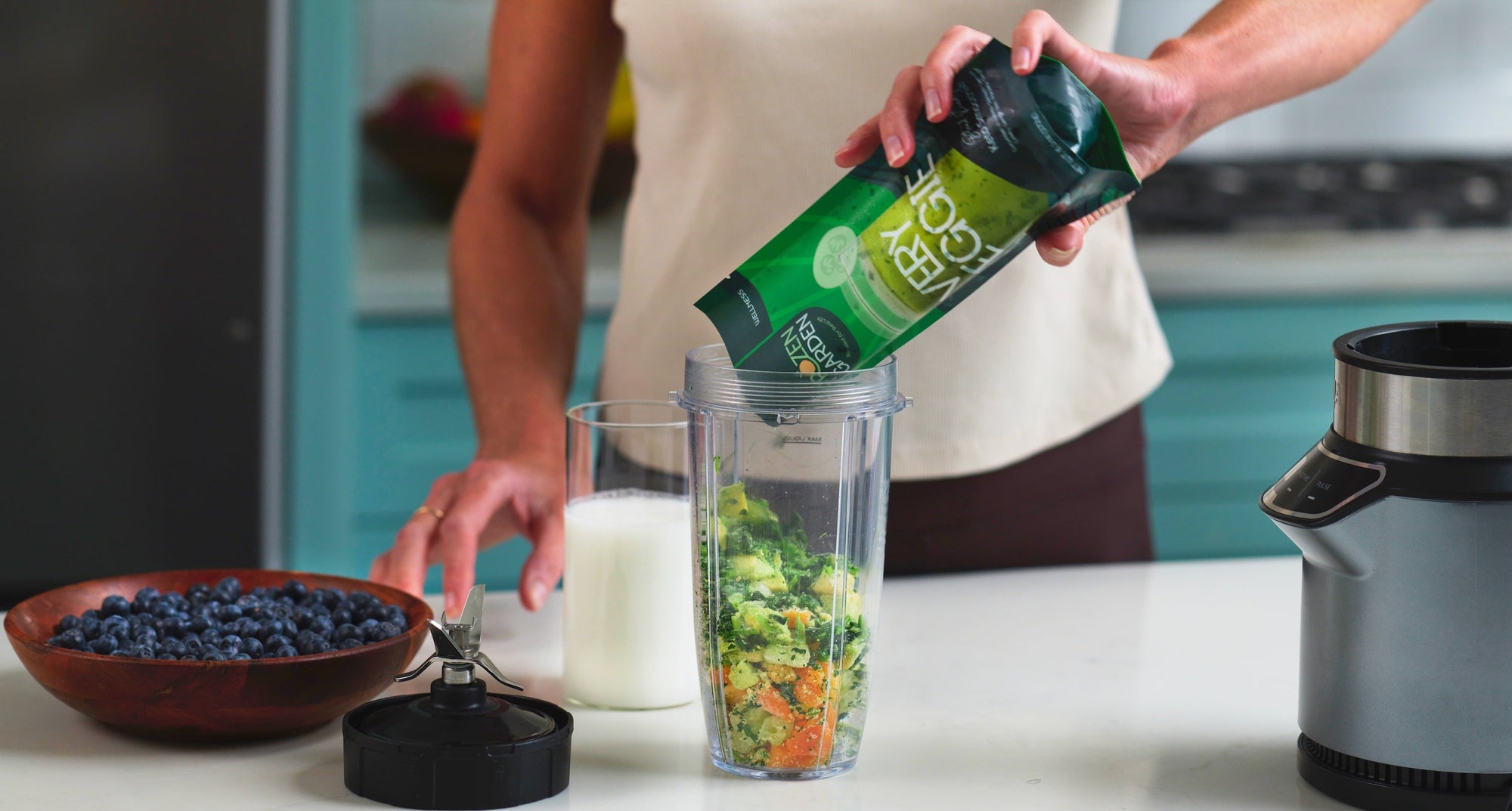 Woman pouring Frozen Garden's ready to blend frozen smoothie packs from her smoothie delivery into a blender.