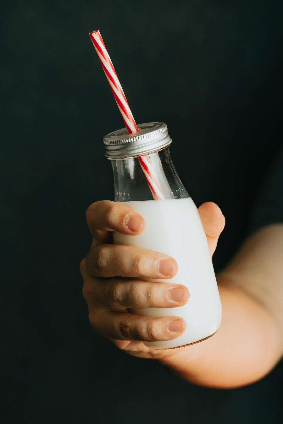 Hand holding a glass bottle of milk with a red and white straw