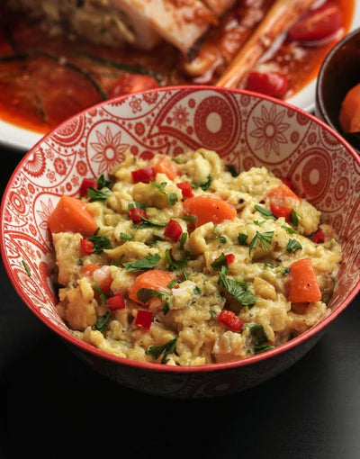 Bowl of scrambled eggs with vegetables in a decorative red and black bowl.
