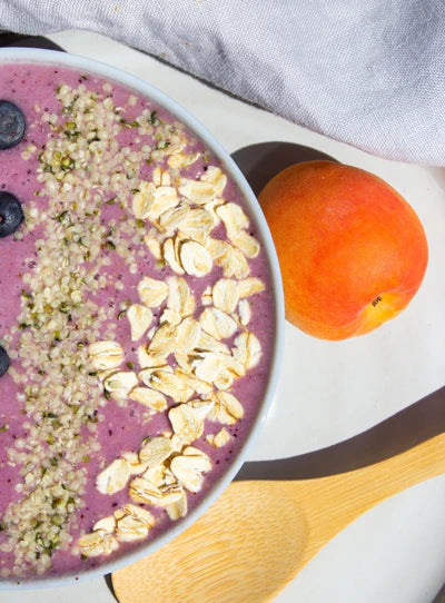 Pink smoothie bowl with oats, seeds, peach slices, and blueberries in a white bowl