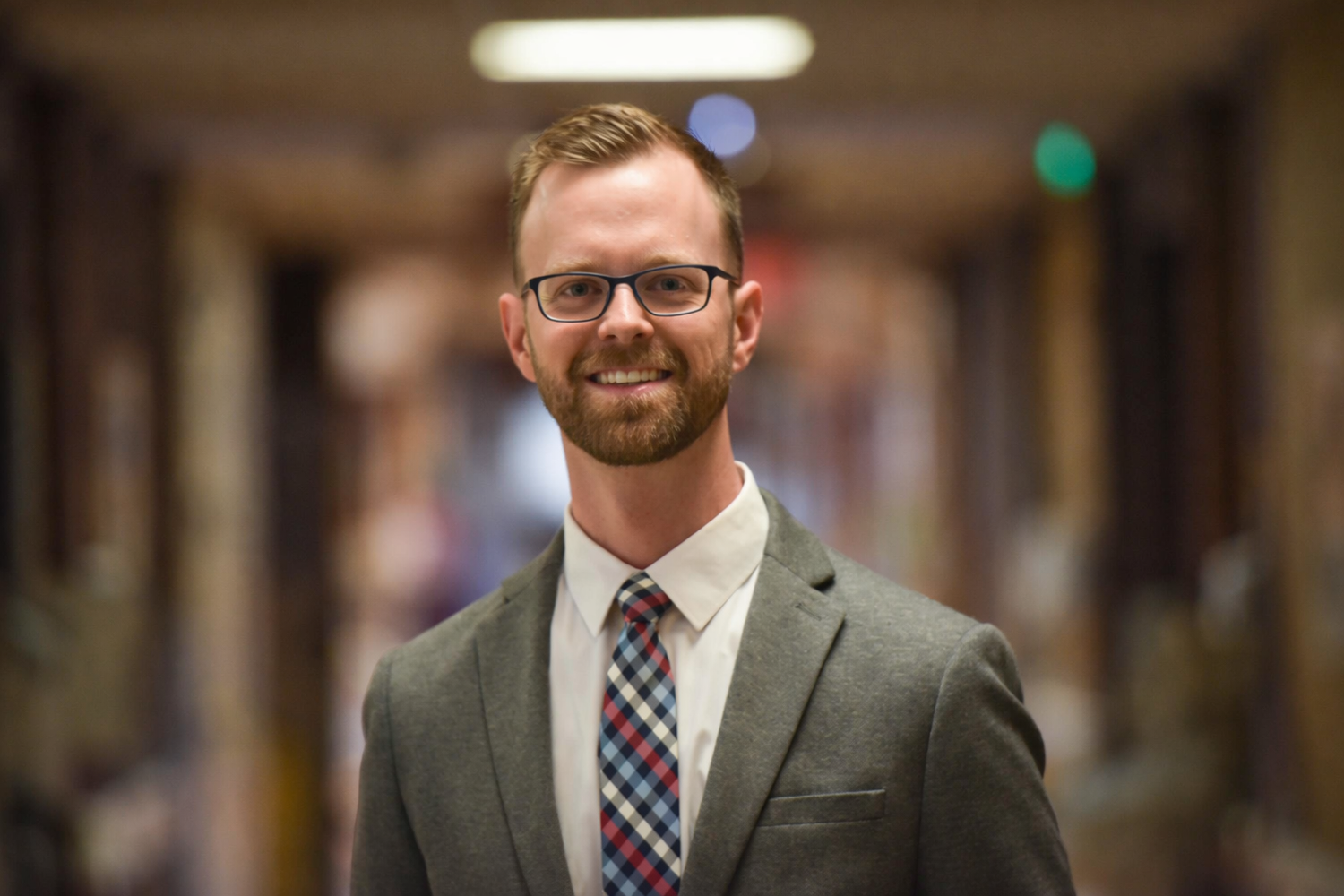 Man (Dr. Ryan Greiner) in a suit and tie standing in a blurred indoor setting