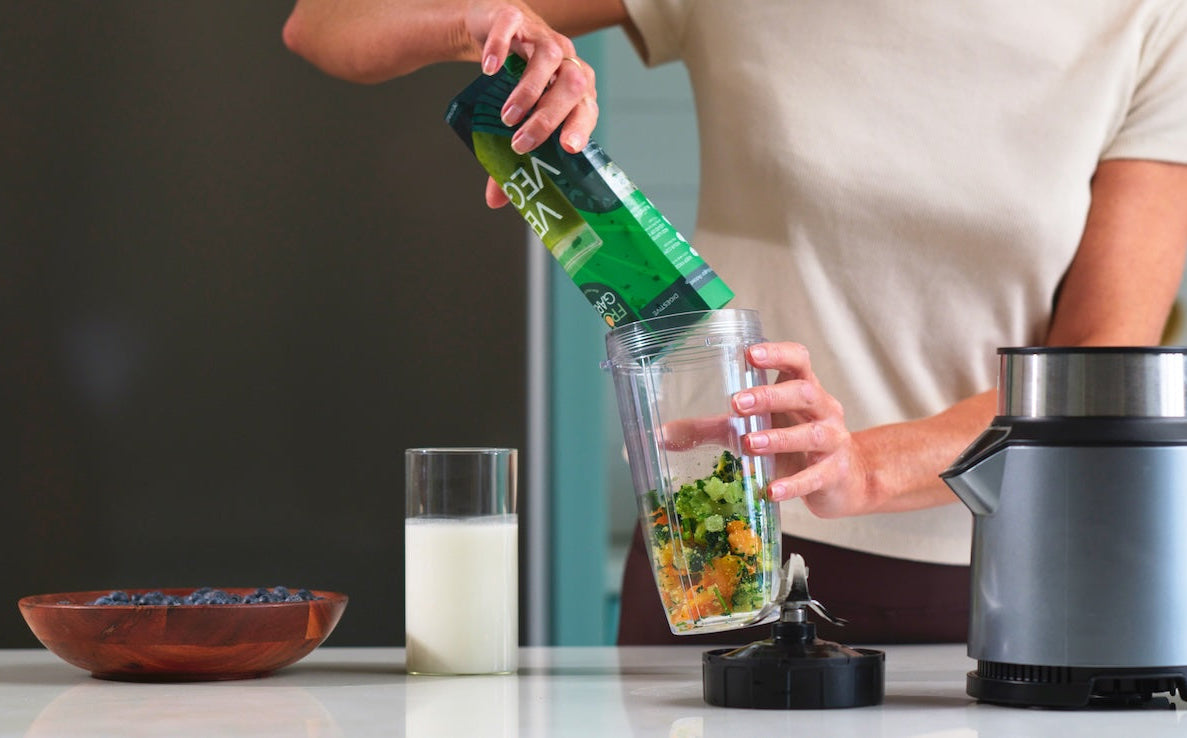 Person using a blender on a kitchen counter with ingredients and a blurred background