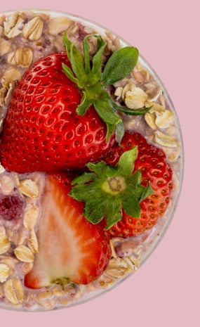 Overhead view of overnight oats topped with fresh whole and sliced strawberries on a pink background