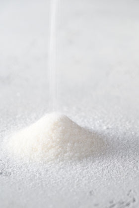 Close-up of a small pile of white sugar crystals on a light gray background