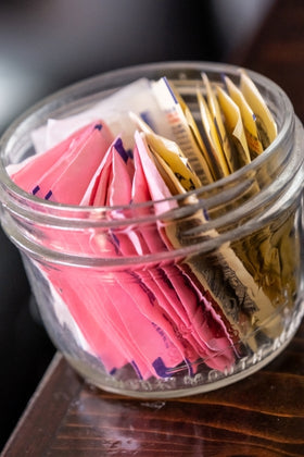 Jar filled with colorful packets of artificial sweetener on a wooden surface