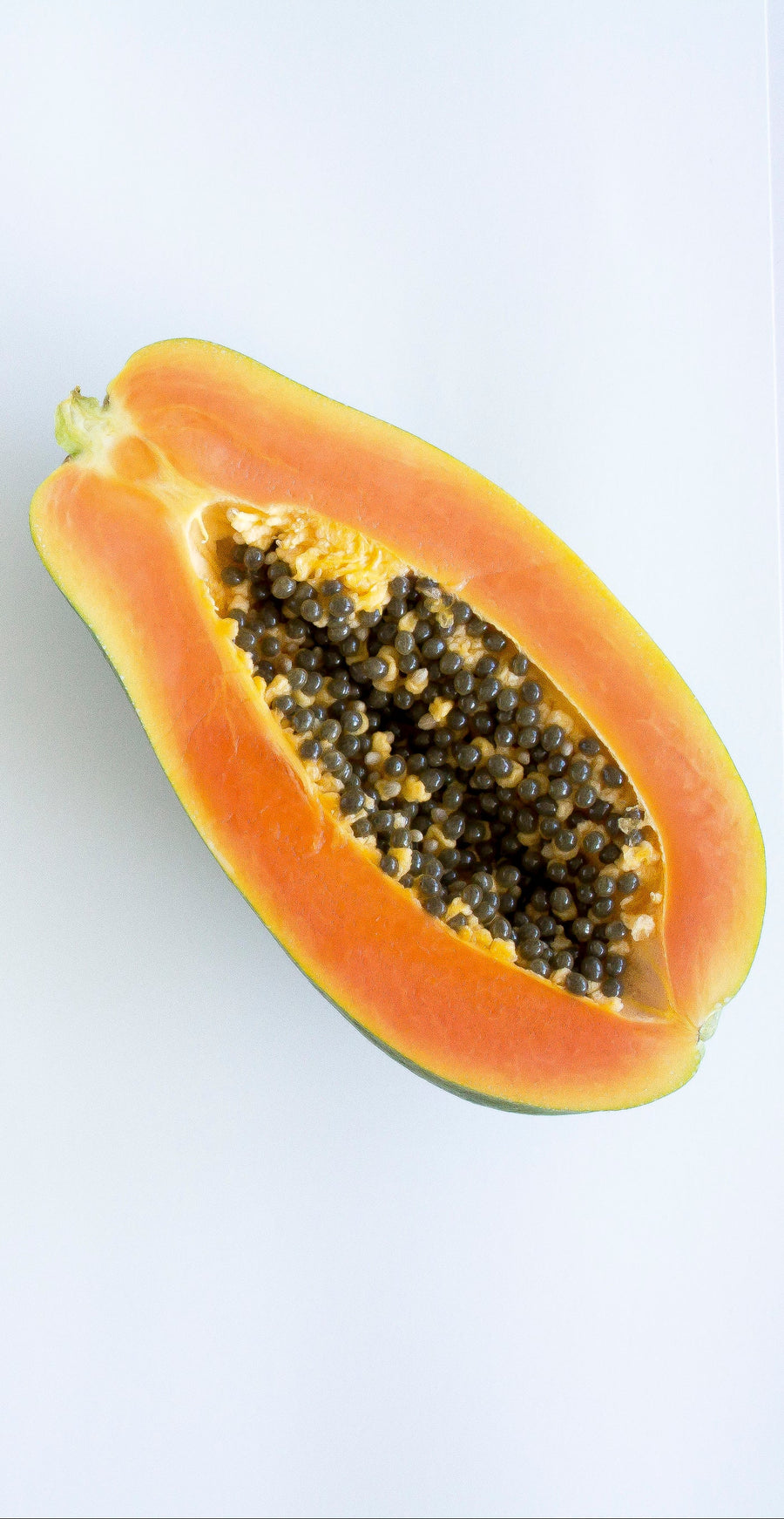 Ripe papaya sliced in half showing bright orange flesh and black seeds on a white background