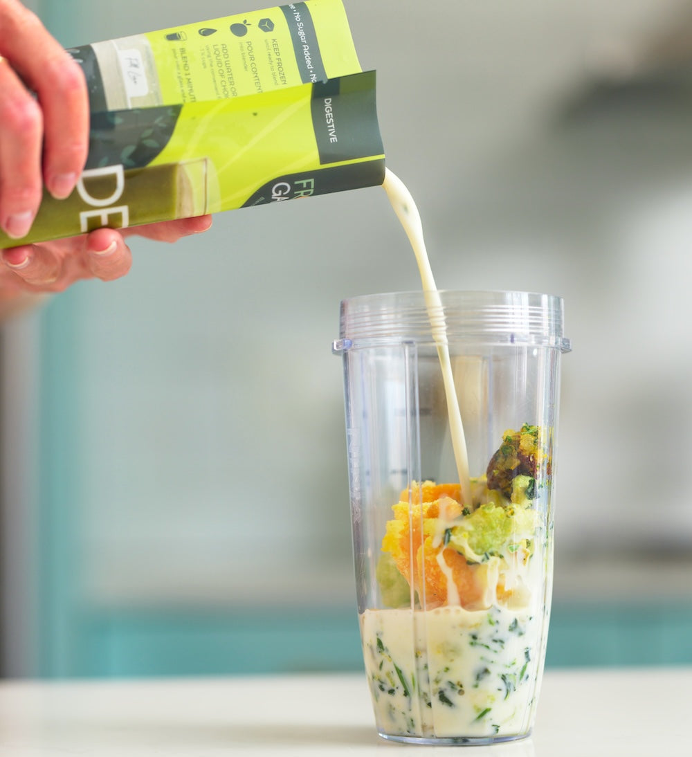 Person pouring a milk into a blender with fruits and vegetables.